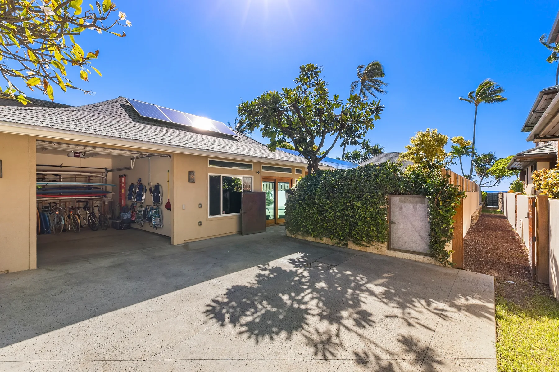A sunny driveway beside a house, with an open garage and leafy trees.