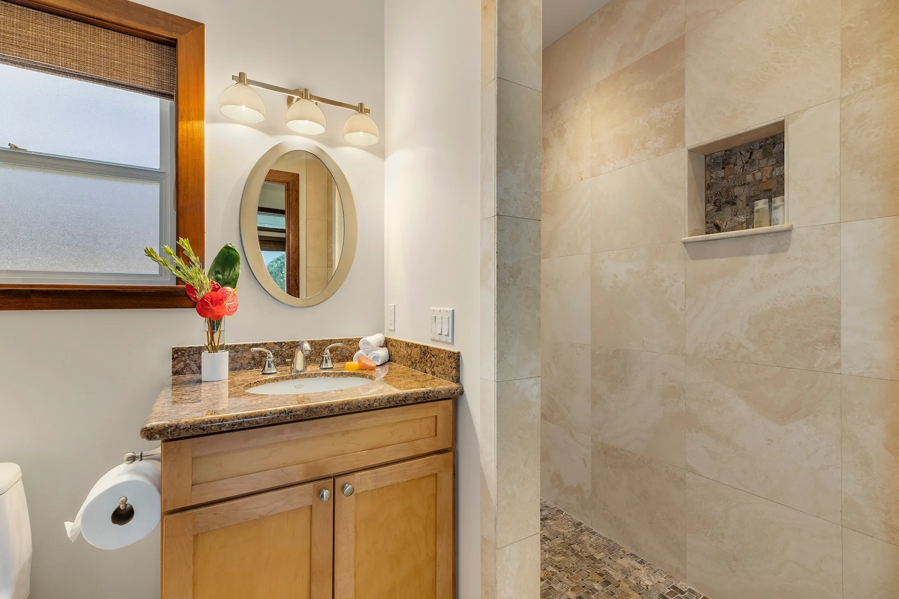 A bathroom vanity with a round mirror sits beside a tiled shower.