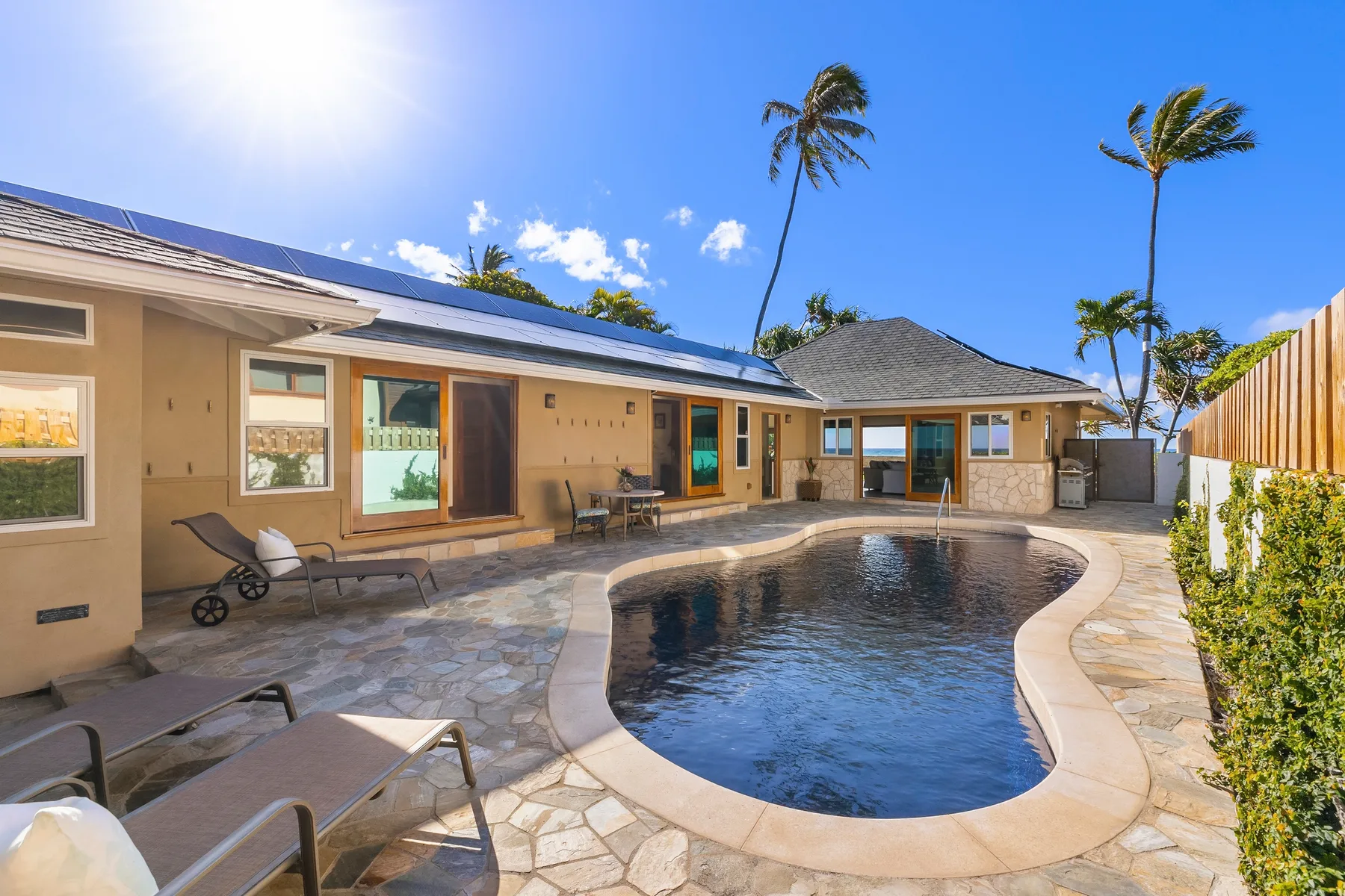 A curved swimming pool sits beside a low building and paved patio.