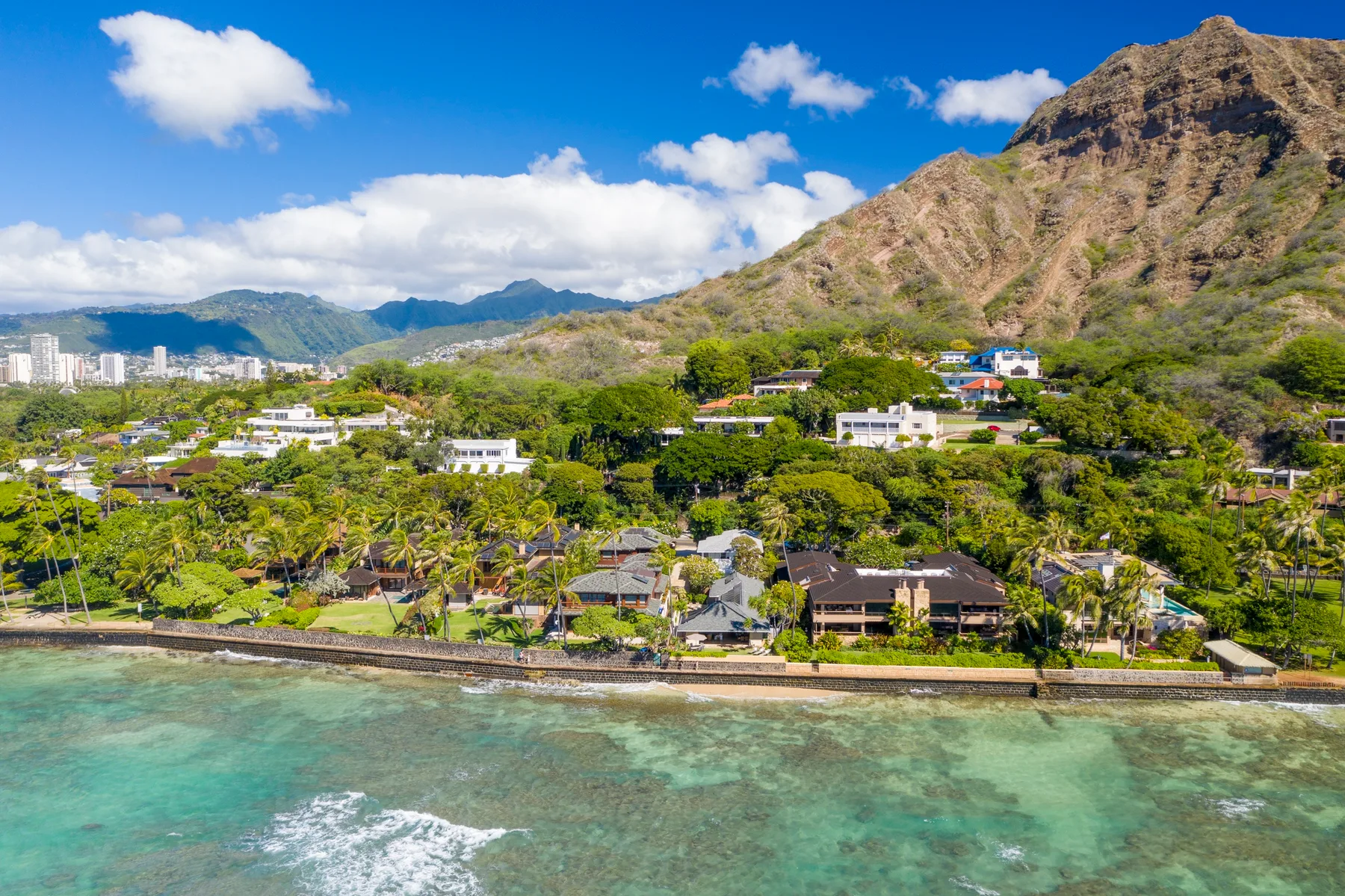 A coastal neighborhood sits between clear turquoise water and a green mountain slope.