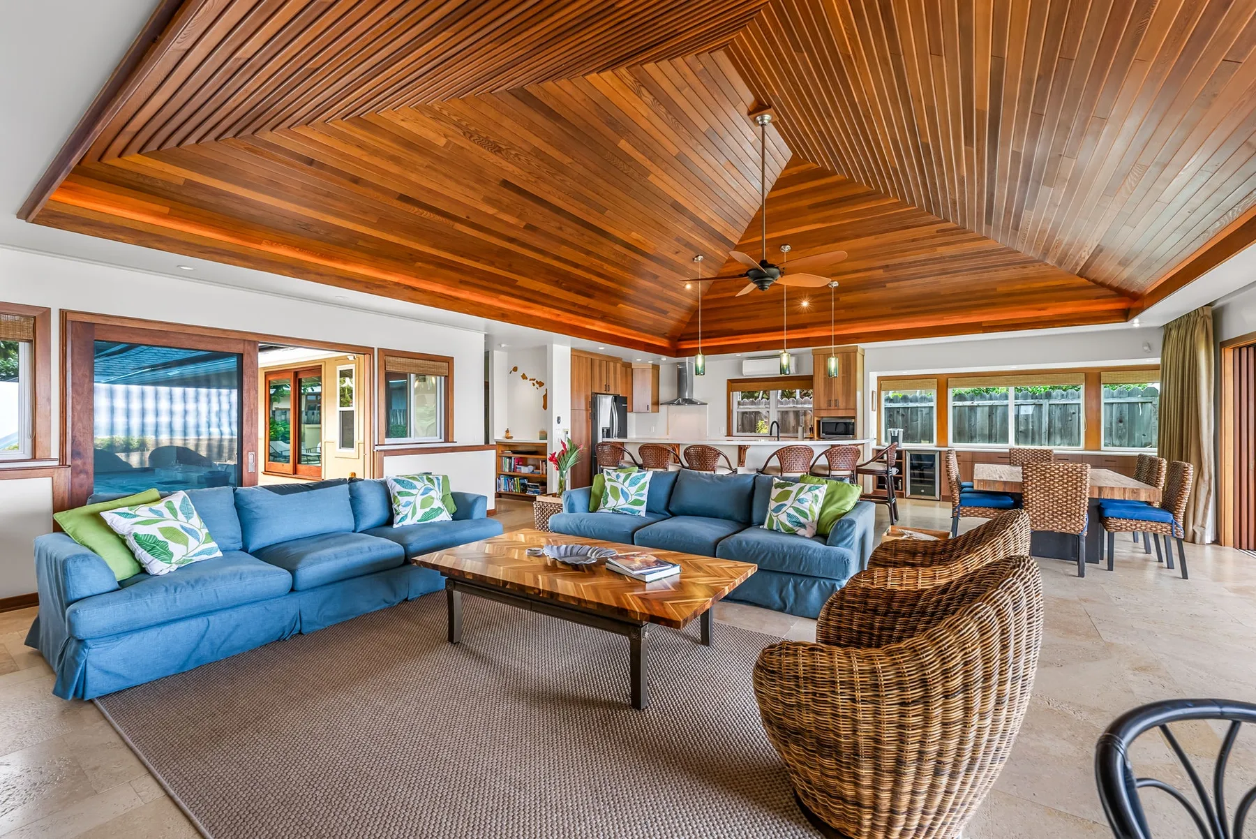 A spacious living and dining area with blue seating beneath a wood-paneled ceiling.