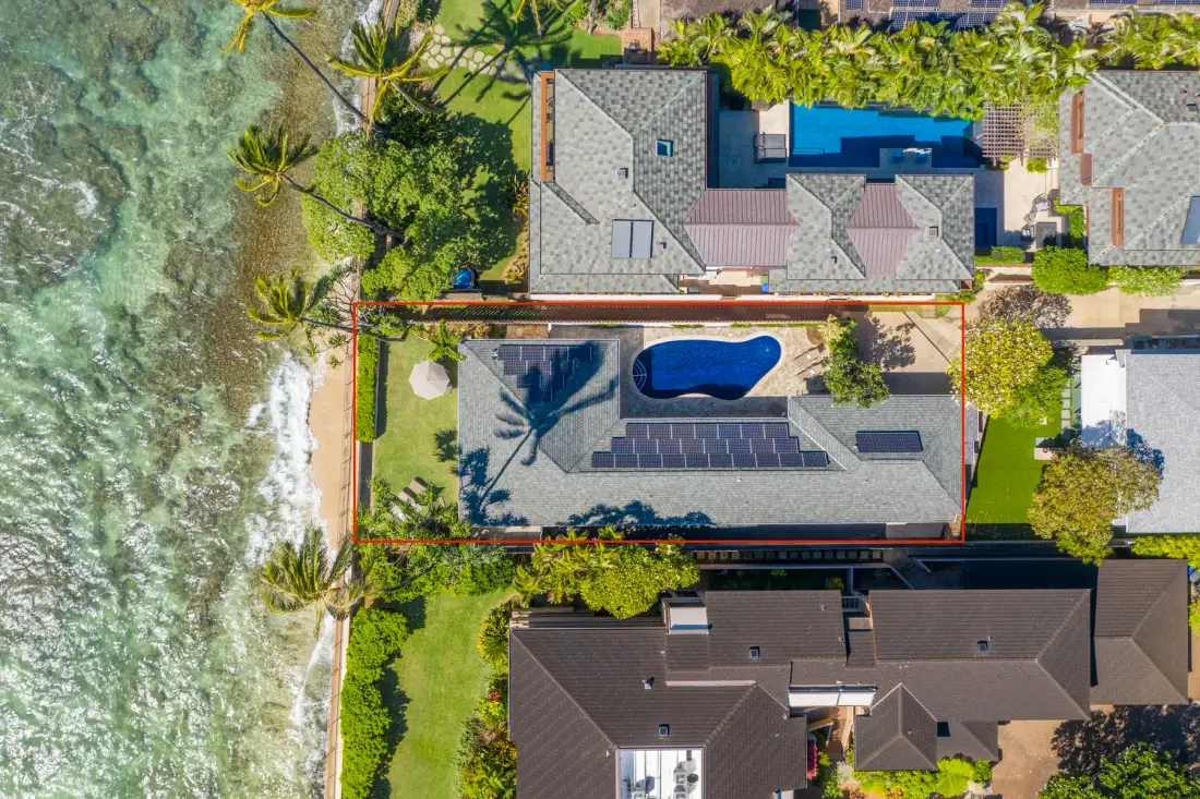 An aerial view shows a coastal property with a pool and surrounding greenery.