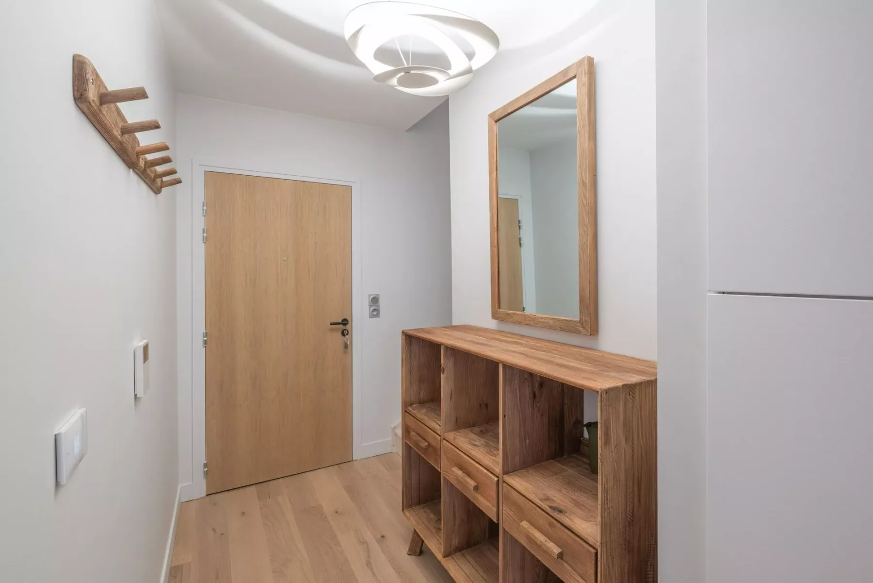 An apartment entryway with a wooden door and a wooden console beneath a mirror.