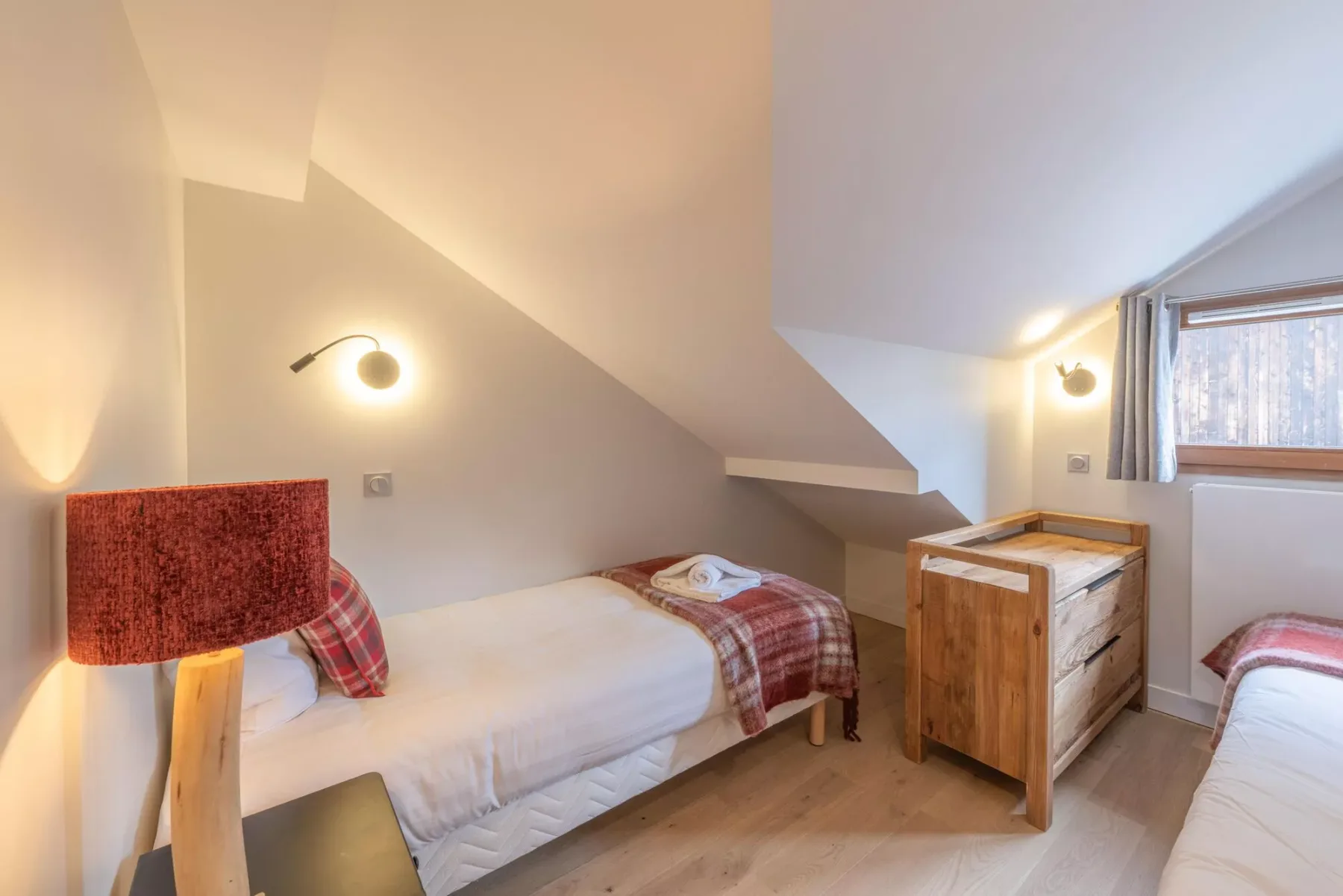 A bright attic bedroom with beds, sloped ceilings, and a window.