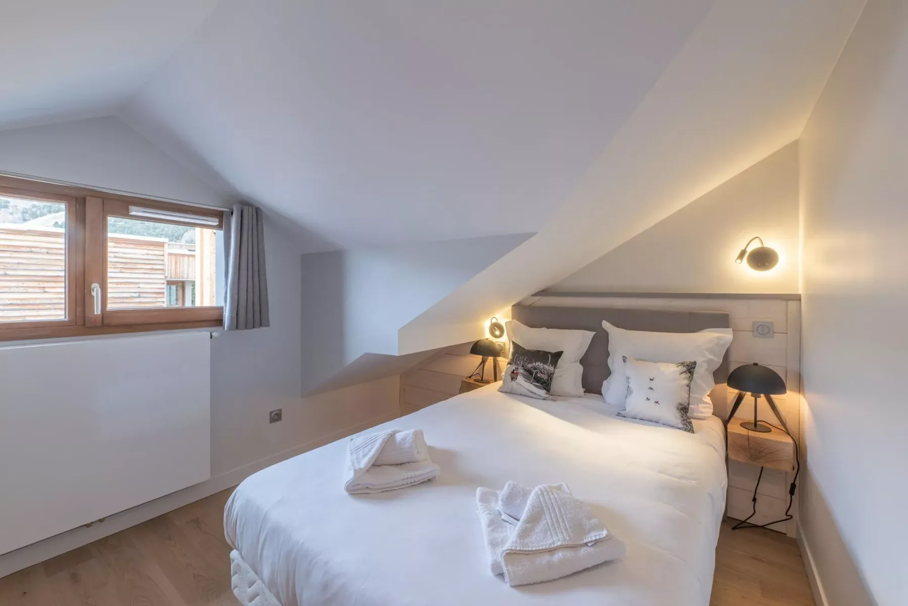 A bedroom with a double bed beneath a sloped ceiling and a window.