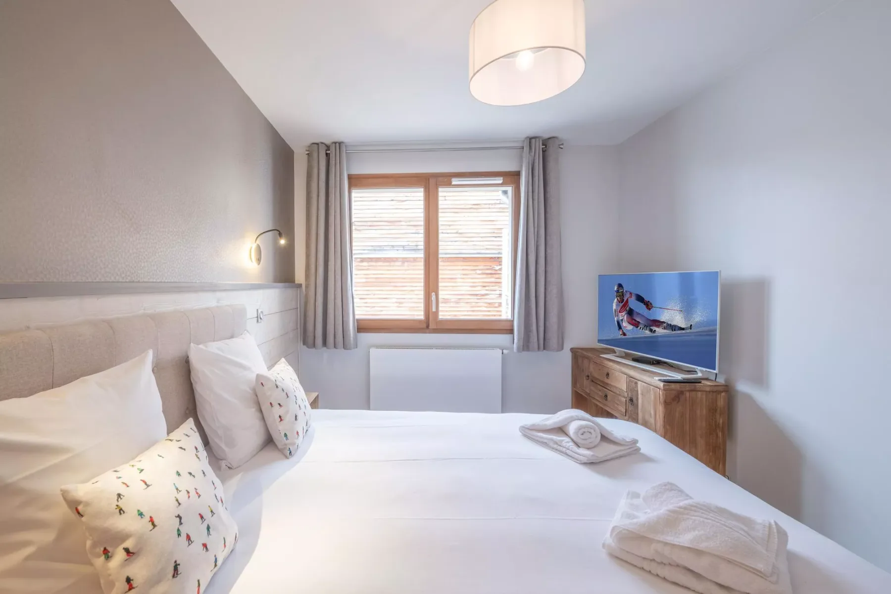 A bedroom with a large bed, a window, and a television on a wooden cabinet.