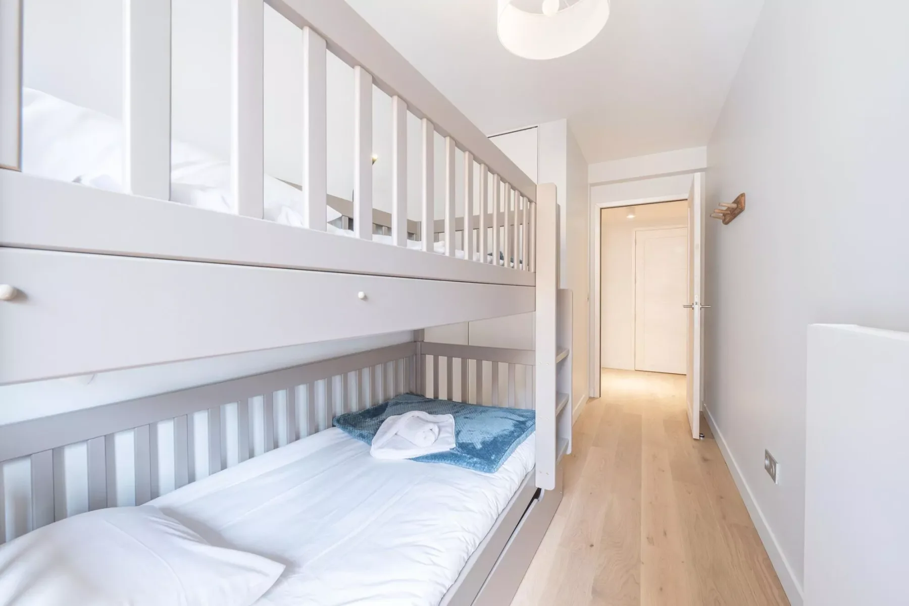 A bright bedroom with white bunk beds and a hallway leading to an open doorway.
