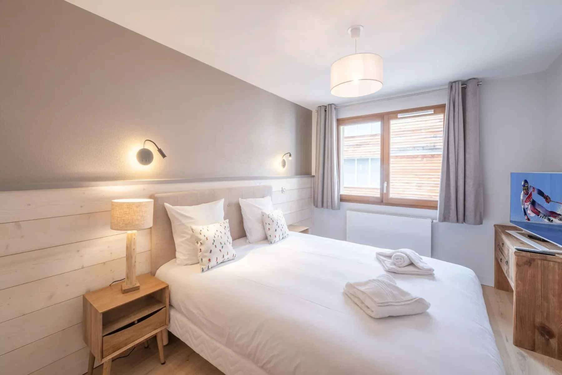 A bright bedroom with a double bed, bedside lamps, and a window.
