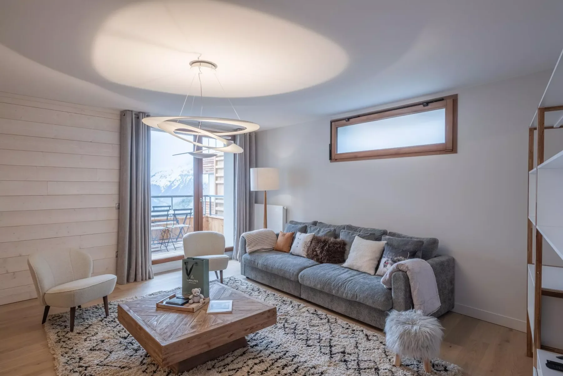 A living room with a gray sofa, a coffee table, and windows overlooking snowy mountains.