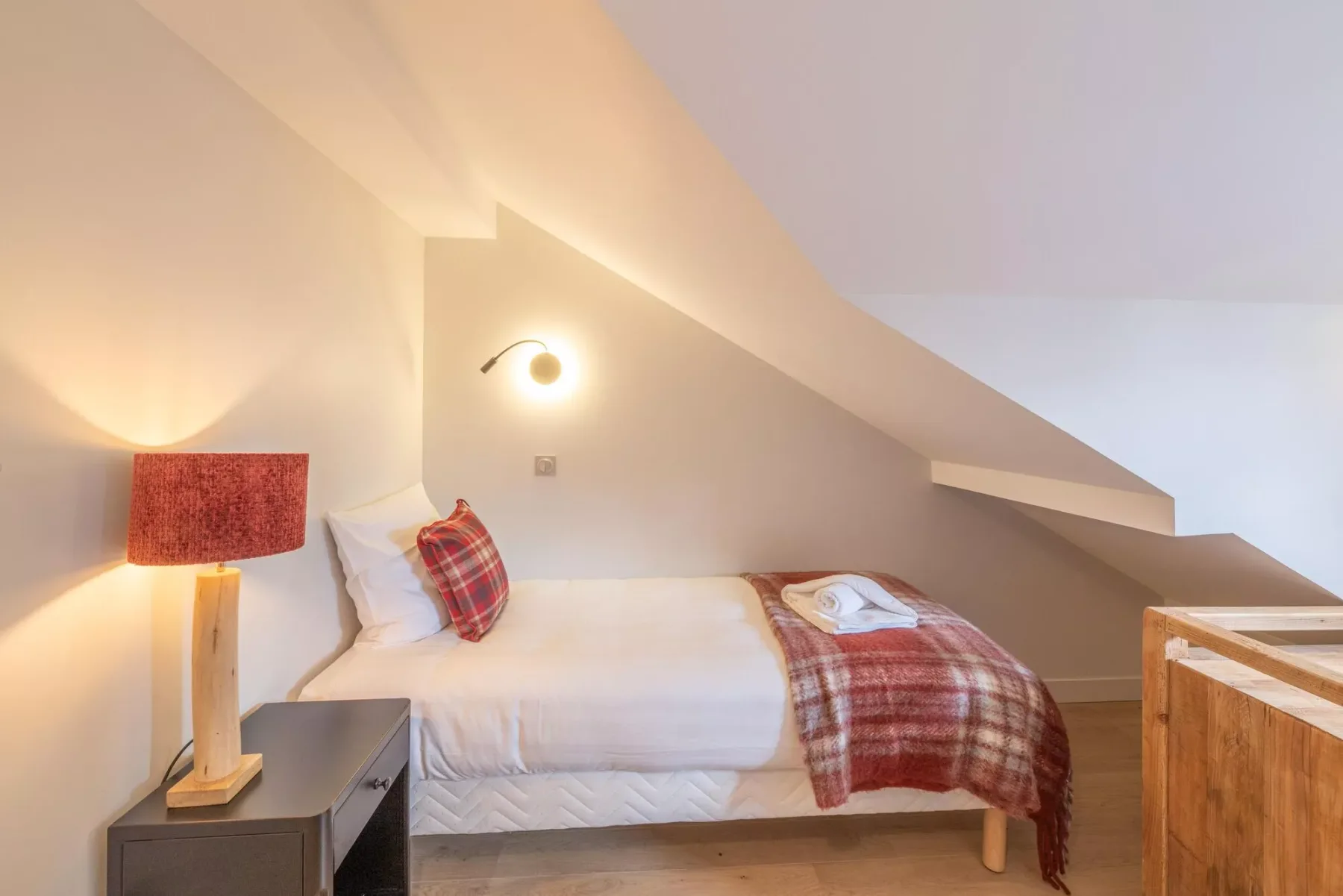 A bedroom with a bed beneath a sloped ceiling and a bedside lamp.