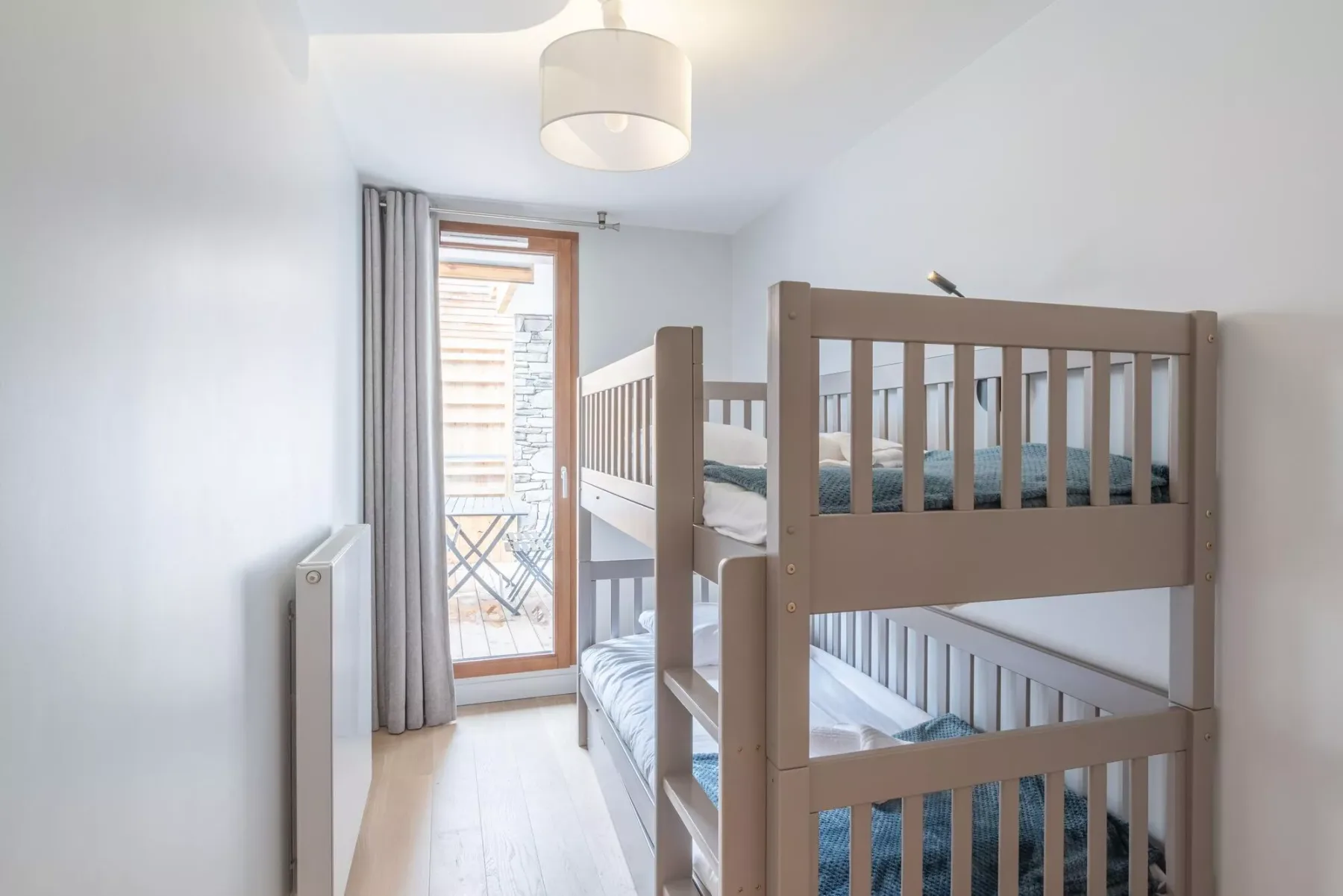 A bright bedroom with a wooden bunk bed beside a glass balcony door.