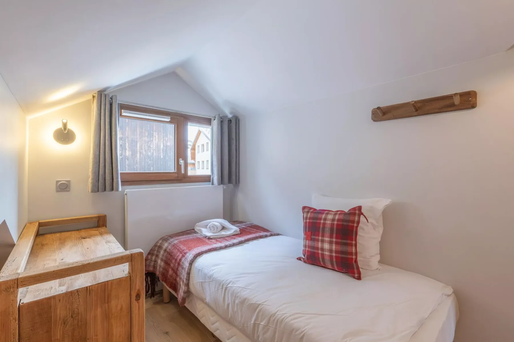 A bedroom with a single bed and a window overlooking nearby buildings.