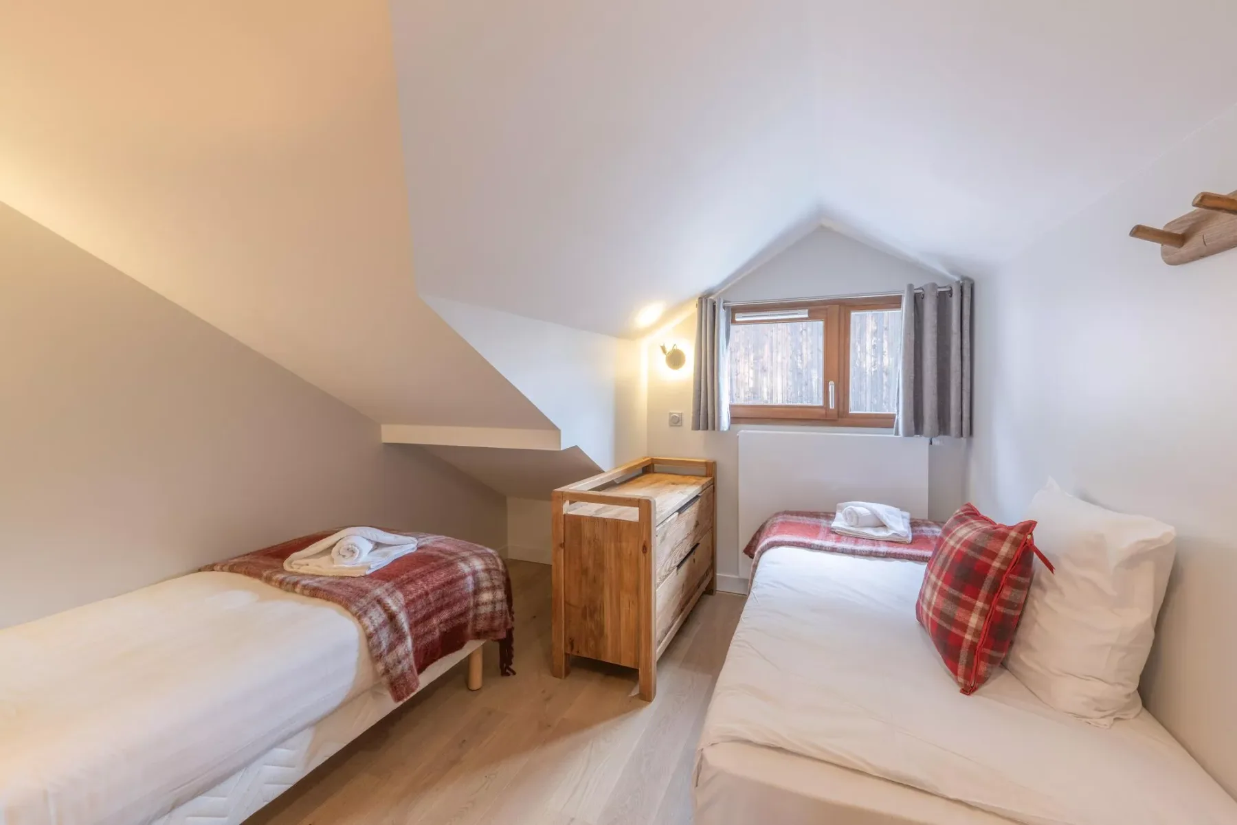 A small bedroom with two single beds, a wooden dresser, and a window.