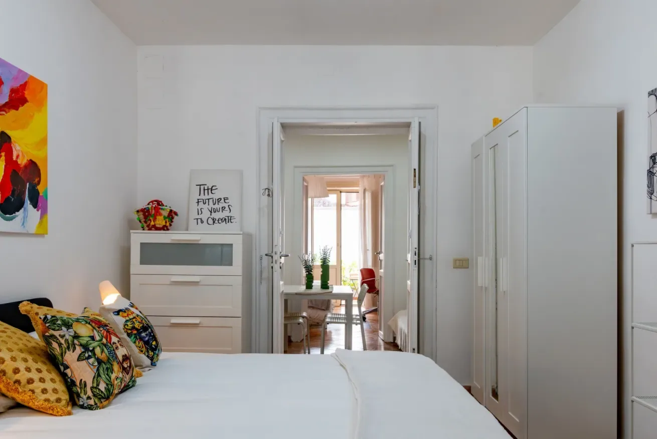 Un dormitorio con una cama y una puerta abierta hacia una habitación contigua luminosa.