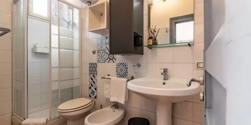 Un baño con azulejos, lavabo, inodoro, bidé y ducha de vidrio.