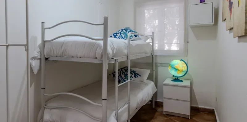 Un dormitorio con una litera metálica y una pequeña mesita de noche.