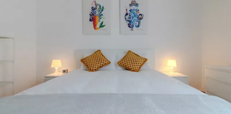 Dormitorio con una cama bien arreglada y dos cuadros coloridos sobre el cabecero.