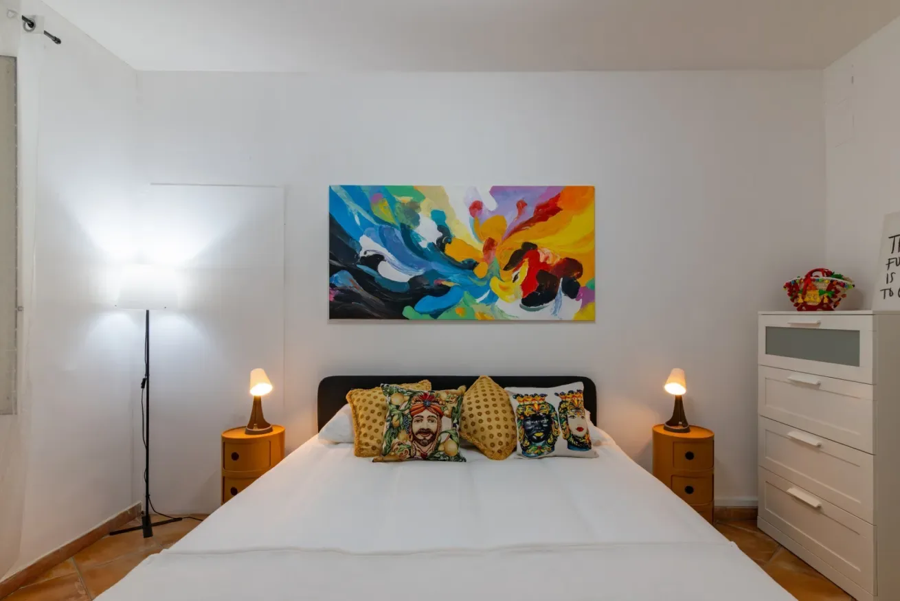 Un dormitorio con una cama bien tendida y una colorida obra abstracta encima.
