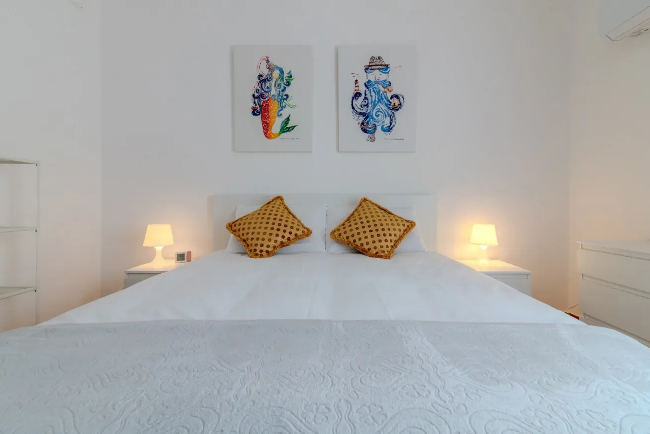 Un dormitorio con una cama bien tendida, lámparas de noche a juego y arte colorido.