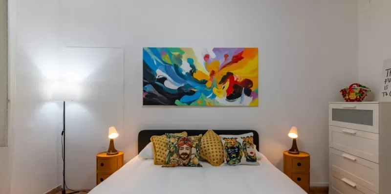 Un dormitorio con una cama bajo una colorida pintura abstracta.