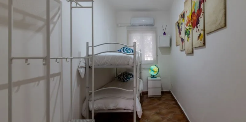 Un dormitorio con una litera metálica, cuadros coloridos y una pequeña mesa de noche.