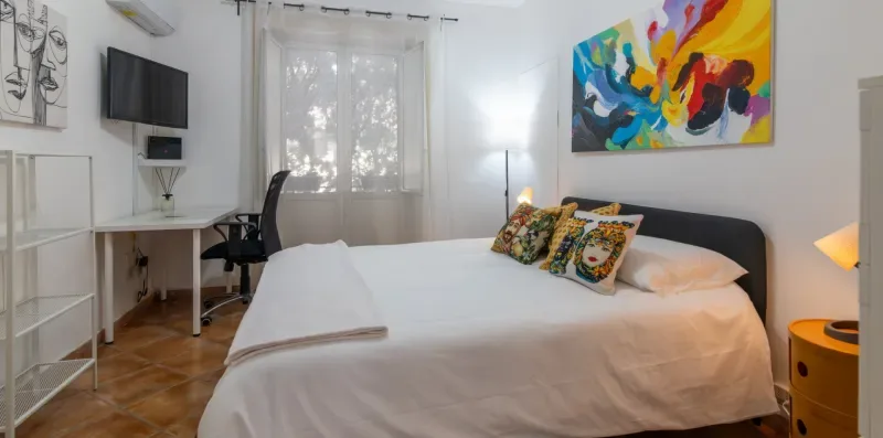 Un dormitorio con una cama bien arreglada y una obra colorida sobre el cabecero.