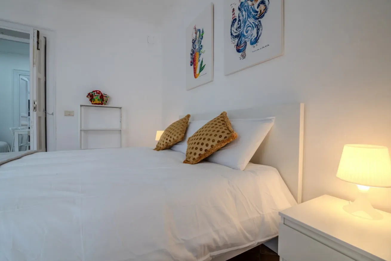 Un dormitorio luminoso con una cama tendida y obras de arte enmarcadas.