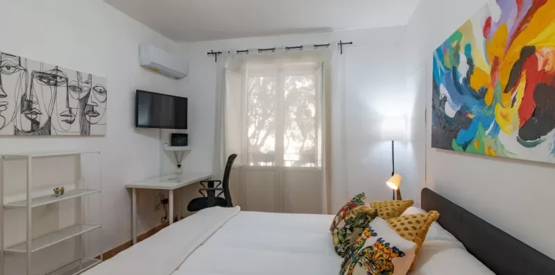 Un dormitorio luminoso con una cama, cojines coloridos y arte abstracto.