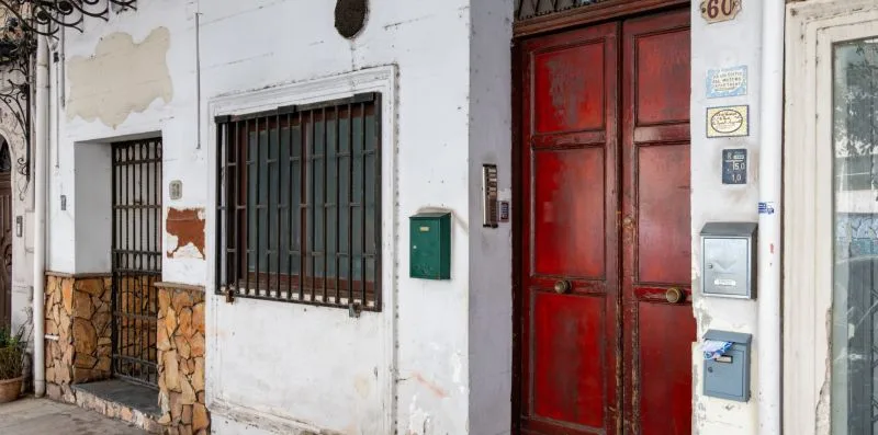 Una fachada blanca con ventanas enrejadas y una puerta de entrada de madera roja.