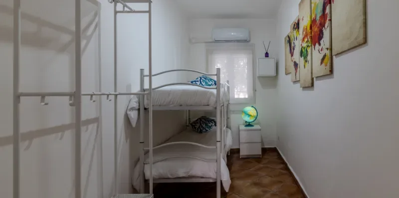 Un dormitorio con una litera metálica, cuadros coloridos y una ventana.