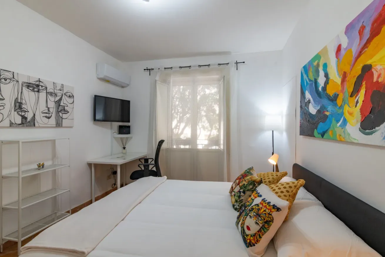 Un dormitorio con una cama, cojines coloridos y obras de arte en las paredes.