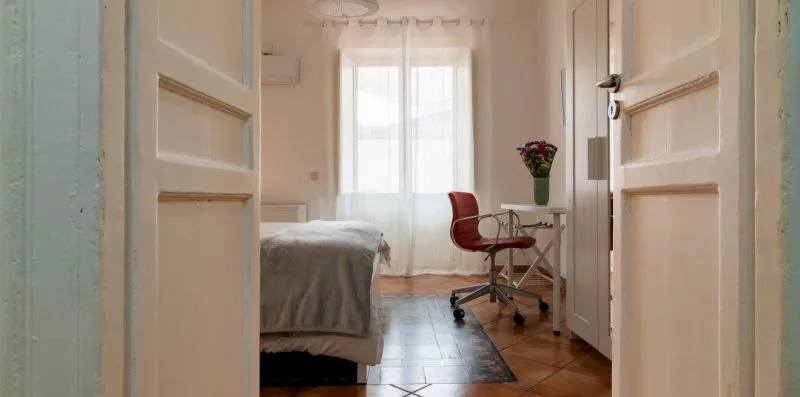 Un dormitorio luminoso con cama, escritorio y silla junto a una ventana.