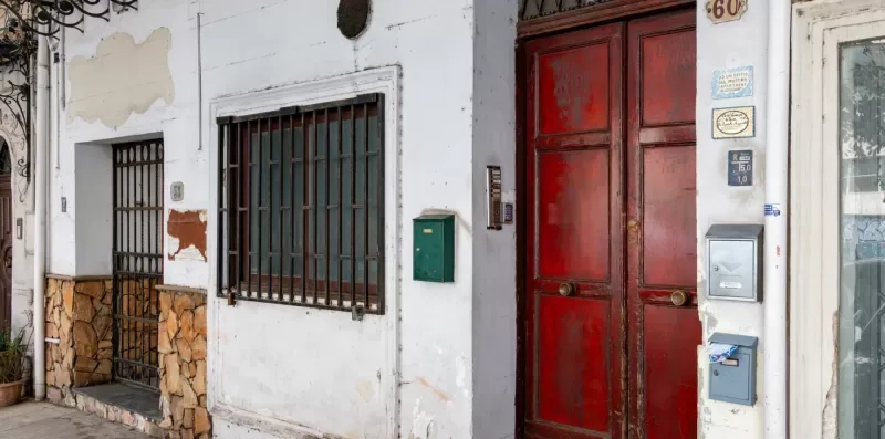 Entrada de un edificio a la calle con una puerta roja y ventanas enrejadas.