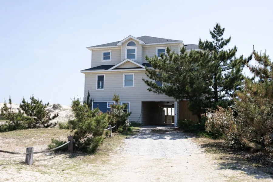 A multi-story house stands at the end of a sandy driveway among trees.