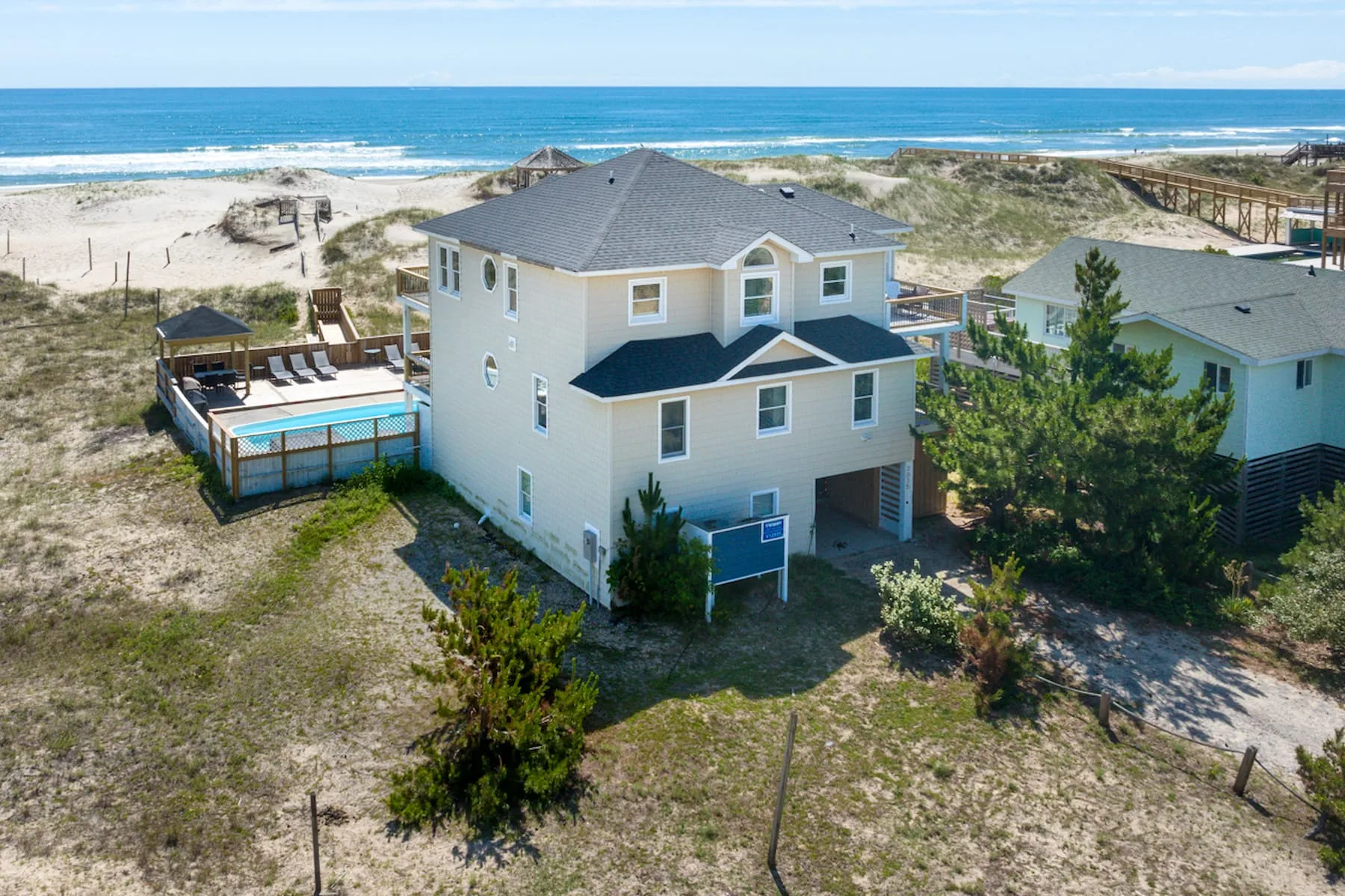 A coastal house stands among sandy dunes beside the ocean.