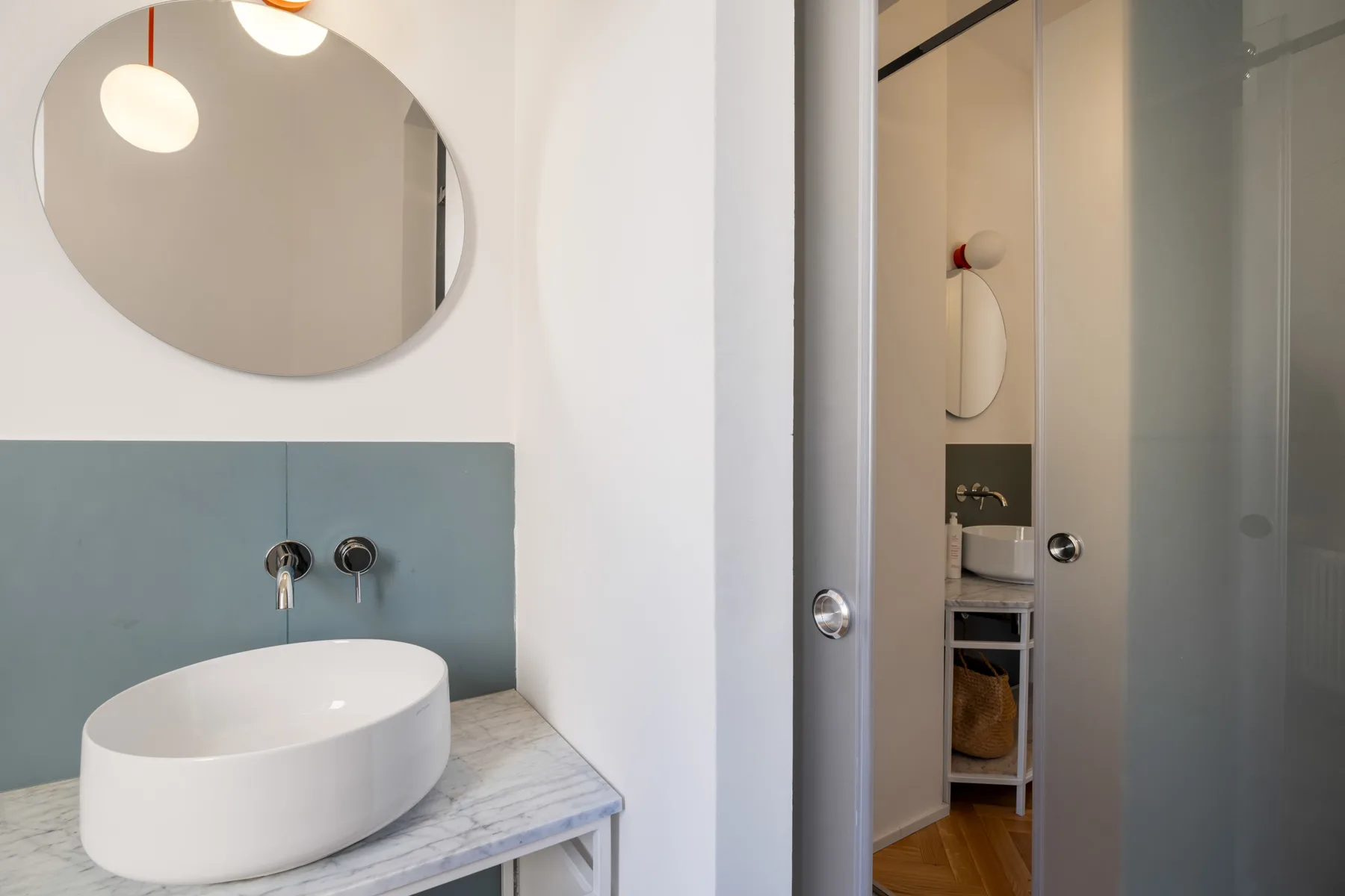 A modern bathroom with a white vessel sink beneath an oval mirror.