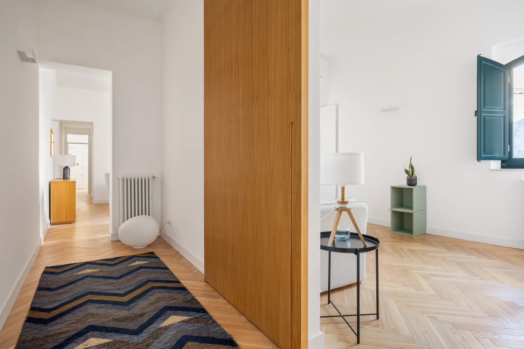 A bright interior hallway opens into a living area with a small table and shelving.