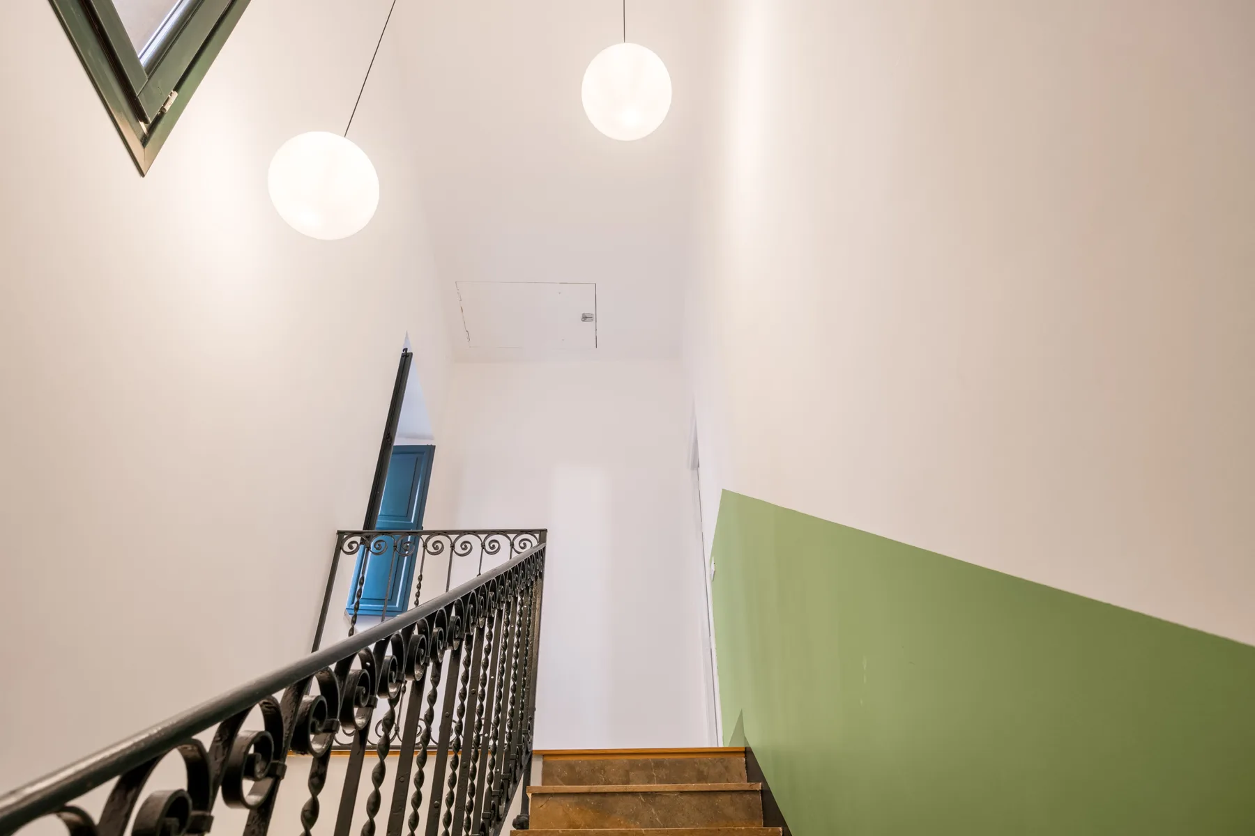 A staircase with ornate dark railings rises beneath two hanging lights.