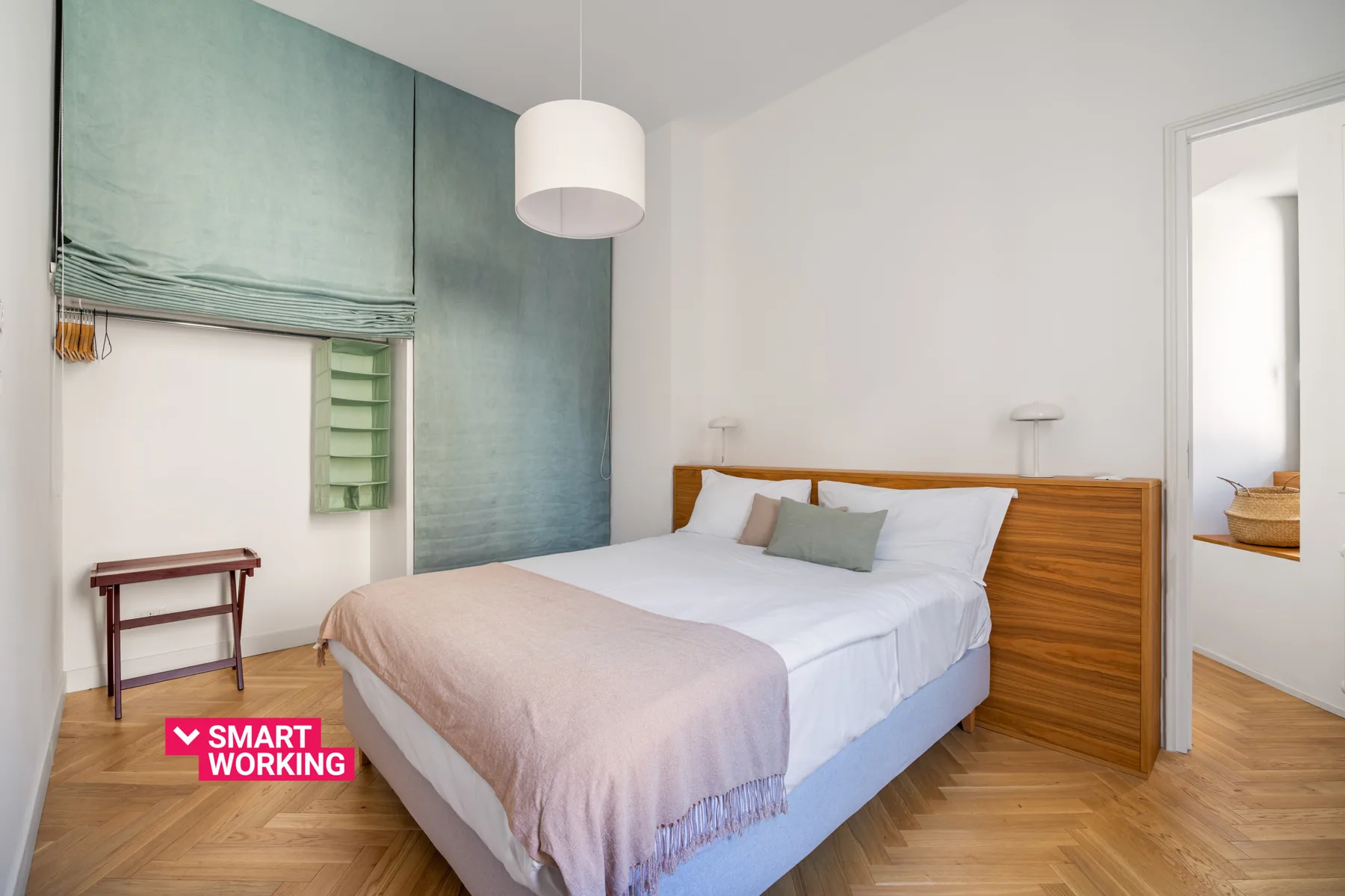 A bedroom with a neatly made bed, a wooden headboard, and a window with a green shade.