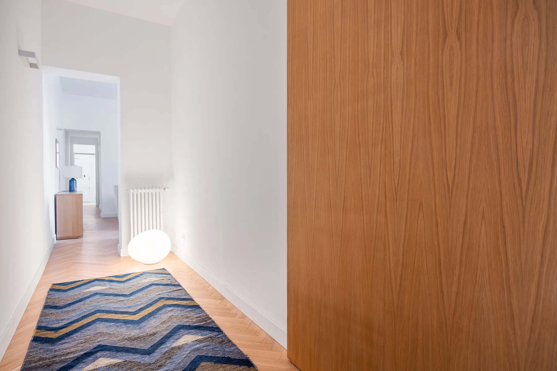 A narrow hallway with a blue patterned rug and a wooden door.
