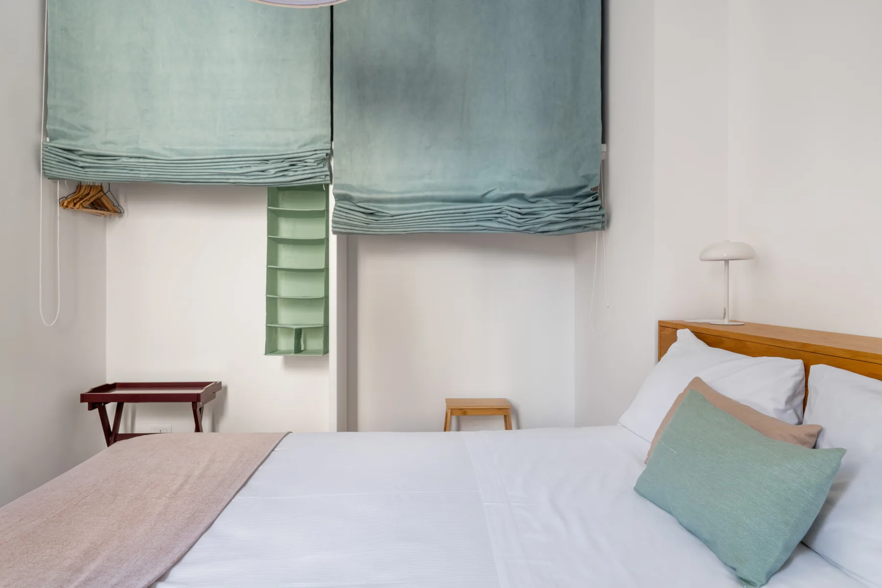 A bedroom with a bed, pale green curtains, and a small bedside lamp.