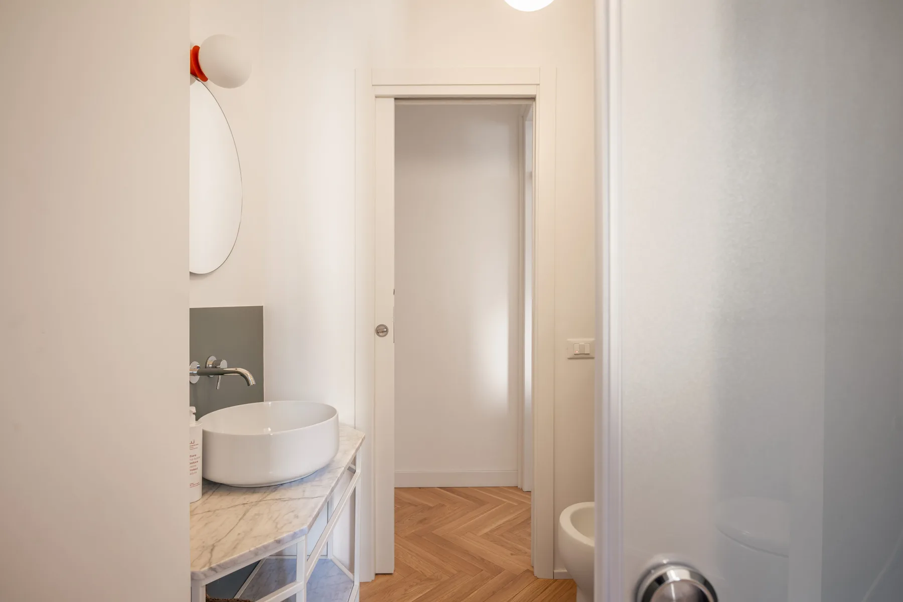 A bright bathroom with a vessel sink and a doorway opening onto a wood-floored hall.