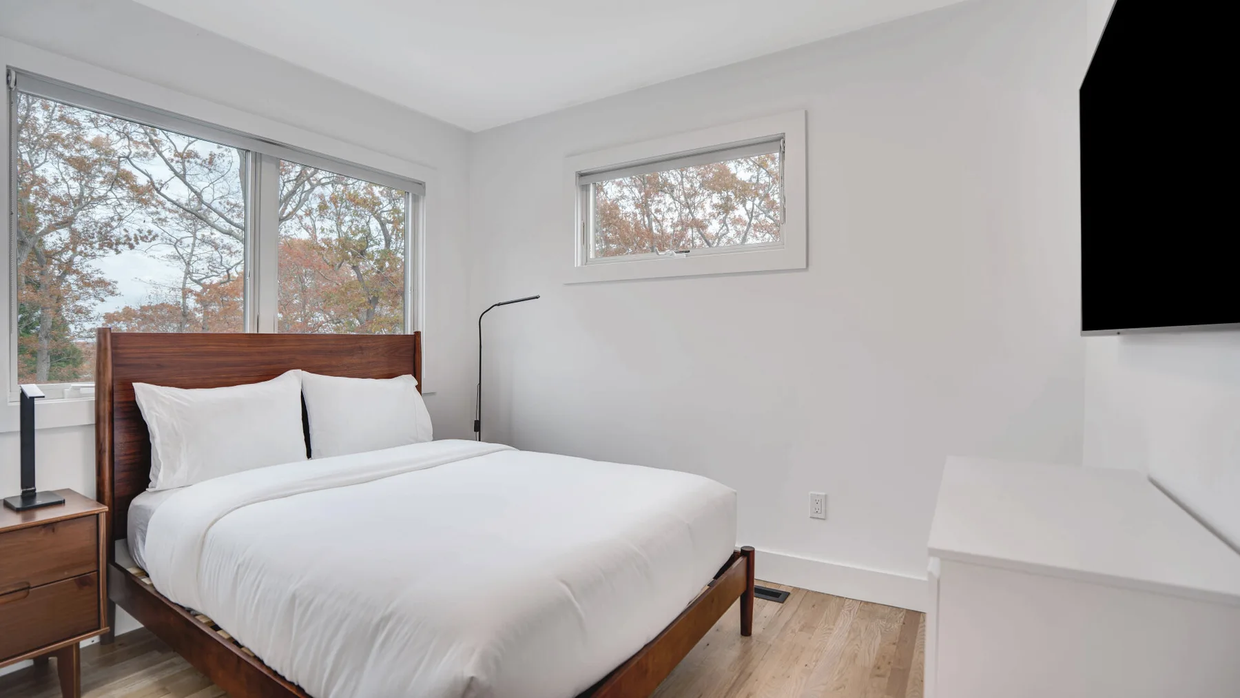 Un dormitorio luminoso con una cama tendida junto a grandes ventanas.