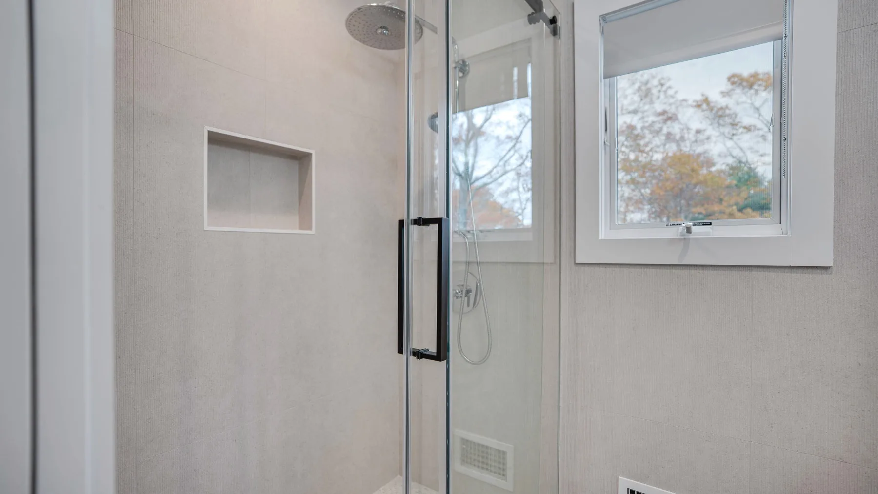 Un baño luminoso con una ducha de vidrio y una ventana con vistas a los árboles.