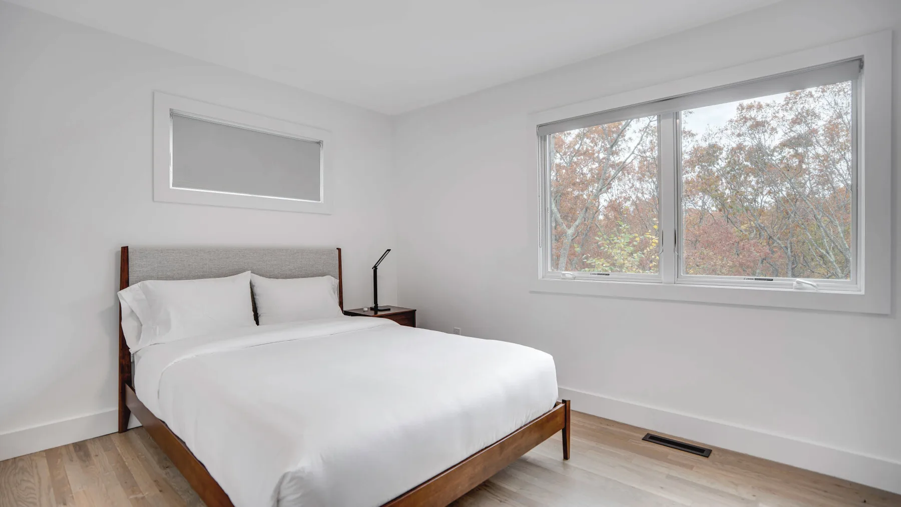 Un dormitorio luminoso con una cama bien tendida y una gran ventana con vistas a los árboles.