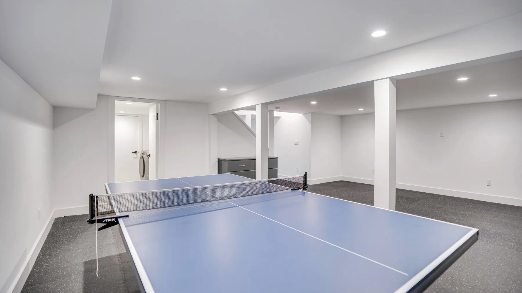 Una sala de recreación en el sótano con una mesa de ping-pong azul y espacio abierto.
