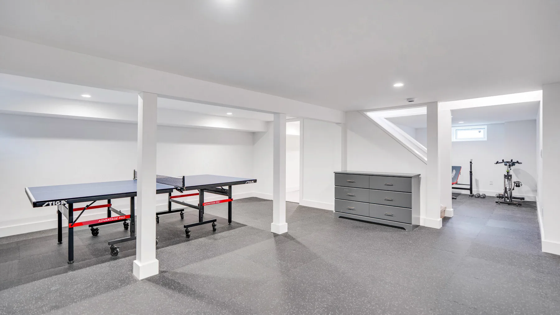 Una zona recreativa en un sótano terminado, con mesas de ping-pong y un armario.