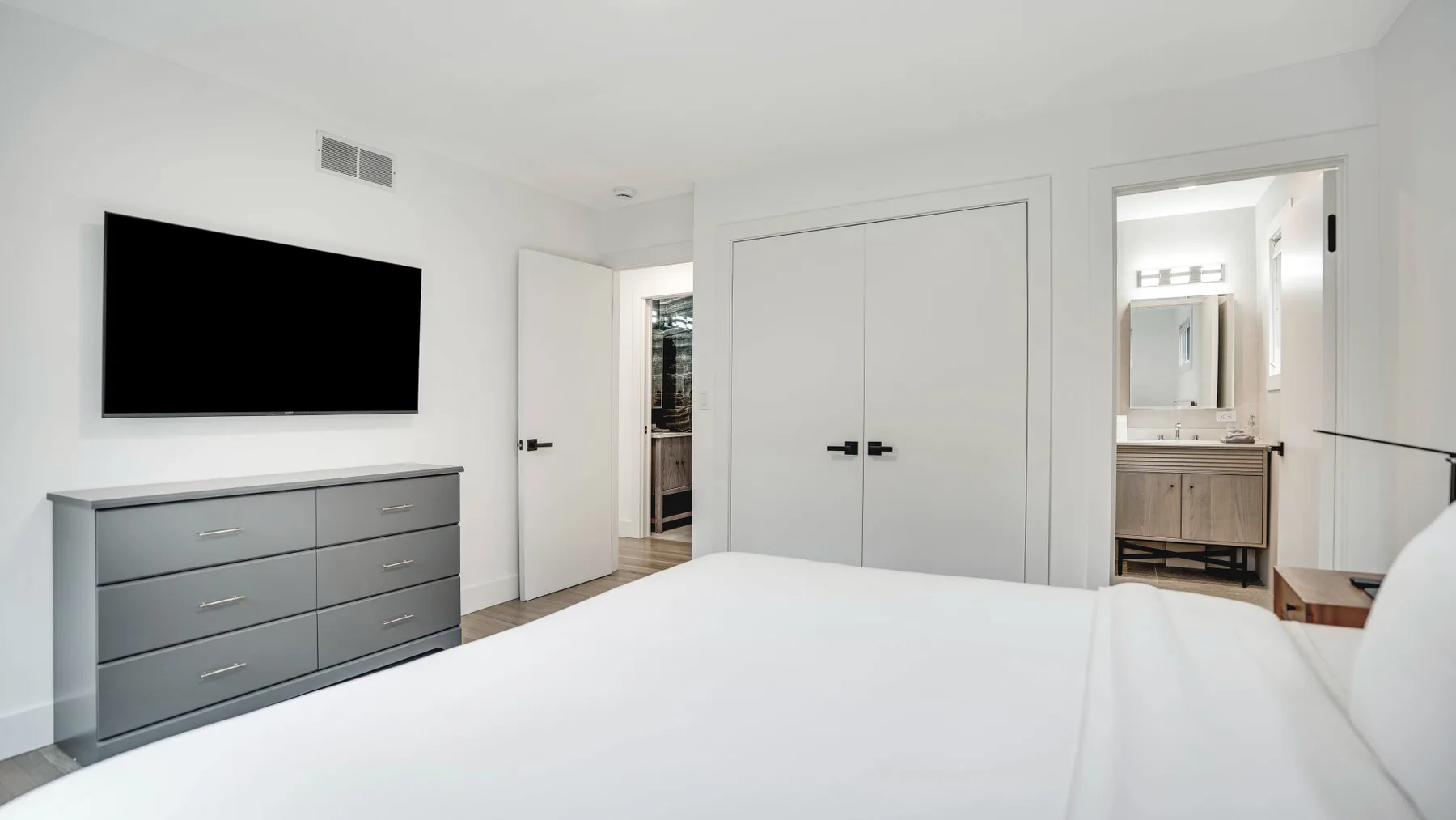 Un dormitorio luminoso con una cama, una cómoda, un televisor en la pared y puertas de armario.