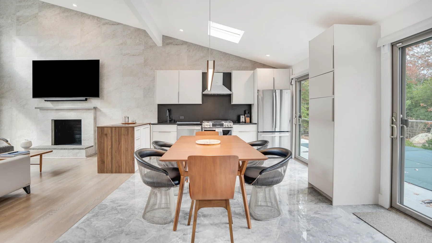 Una cocina abierta al comedor tiene una mesa de madera y amplias puertas de vidrio.