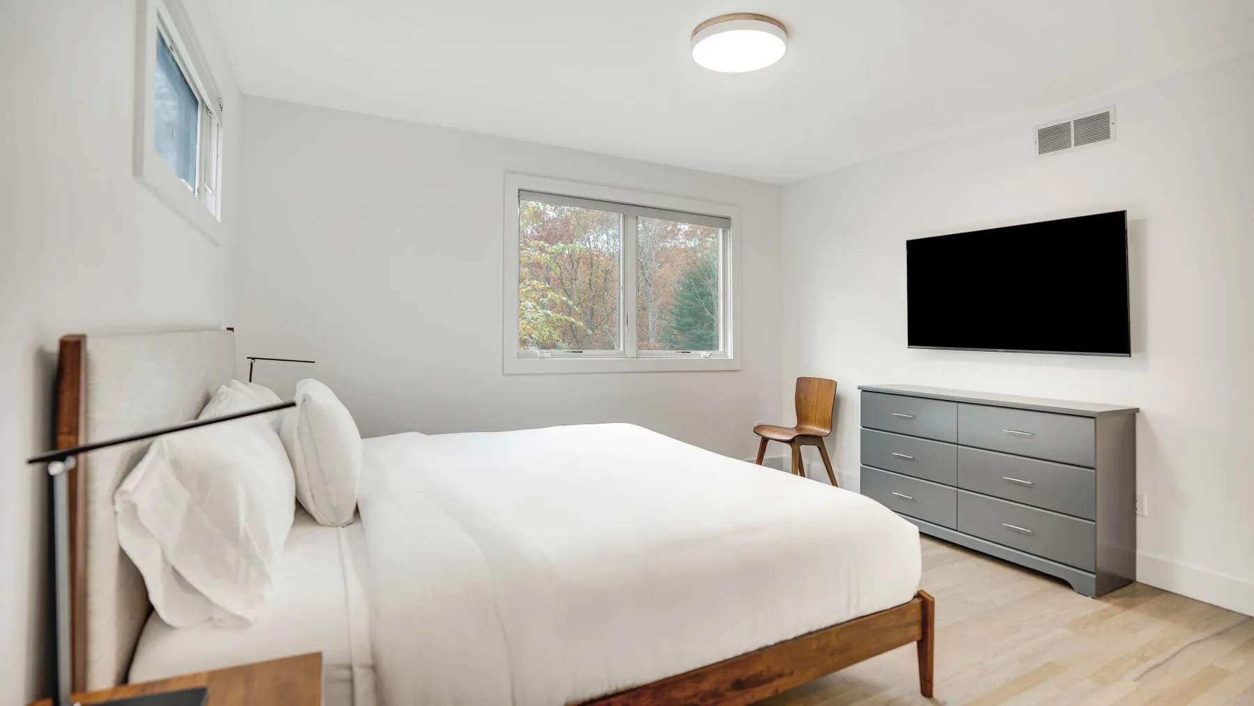 Un dormitorio luminoso con una cama tendida y un televisor sobre una cómoda.